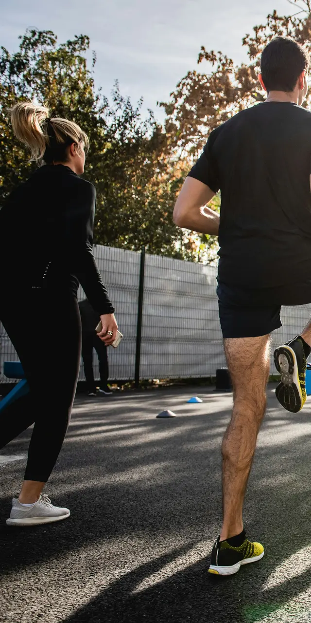 People in workout clothes doing high knees together on an outdoor court in the sun.