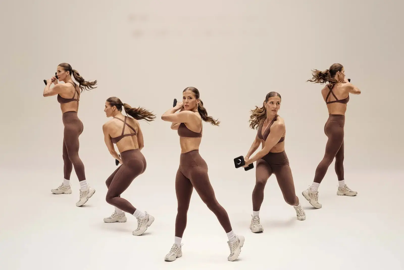 A coach shown five times mid-movement, training with a light dumbbell against a warm studio backdrop.